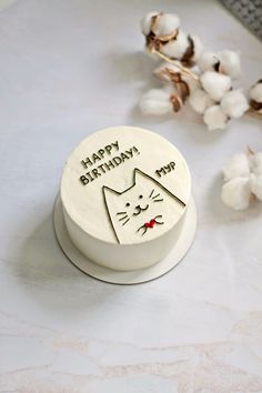 a birthday cake with a cat design on the top and cotton flowers in the background