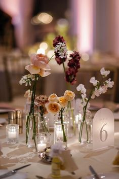 there are many flowers in vases on the table at this wedding reception with candles and place cards