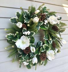 a wreath hanging on the side of a house with white flowers and pine cones around it