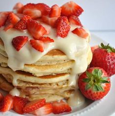 a stack of pancakes topped with strawberries on top of a white plate and drizzled with icing