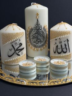 three white candles with arabic writing on them and four stacks of gold coins in the foreground