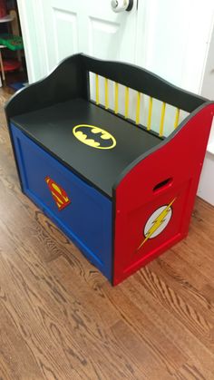 a wooden toy box with batman and superman symbol painted on the sides, sitting in front of a door