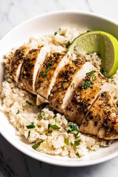 a white bowl filled with rice and sliced chicken on top of it next to a lime wedge