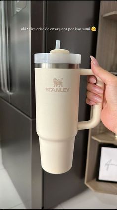 a person is holding a coffee cup in front of a refrigerator with the word stanley on it