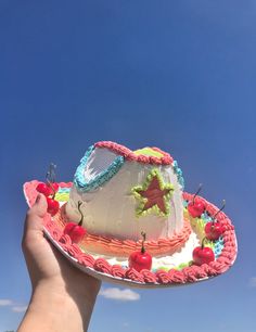 a hand holding up a cake with cherries on it in front of a blue sky