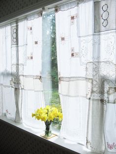 a vase with yellow flowers sitting on a window sill in front of a curtain