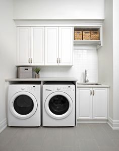 a washer and dryer in a white laundry room with cabinets on the wall