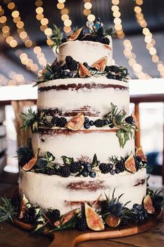 a three tiered cake with fruit and greenery on the top is sitting on a wooden table