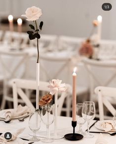 the table is set with white linens, candles and flowers in tall vases