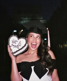 a woman wearing a graduation cap and gown holding a heart shaped cake