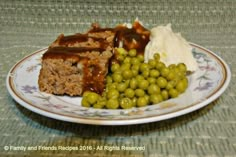 a white plate topped with meatloaf covered in gravy and green peas