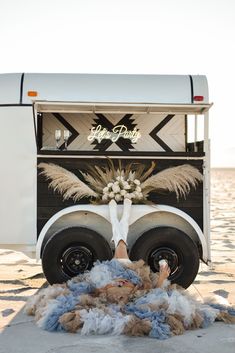 a person laying on the ground in front of a horse trailer with flowers and feathers