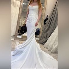 a woman in a white wedding dress standing in front of a mirror and looking at the camera