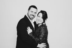 a man and woman hugging each other in front of a white wall with their arms around each other