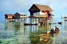 two people in a small boat on the water next to some wooden houses and piers