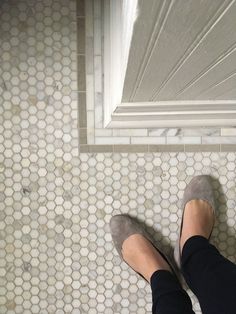 a woman's feet in grey shoes standing on a tiled floor