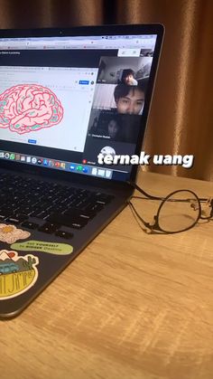 an open laptop computer sitting on top of a wooden desk next to a pair of glasses