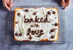 two hands holding a cake with white frosting and chocolate chips on top that says baked with love