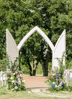 an archway with flowers and greenery on the side is surrounded by white wooden chairs