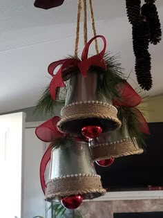 three bells hanging from the ceiling decorated with red bows and pineconis for christmas