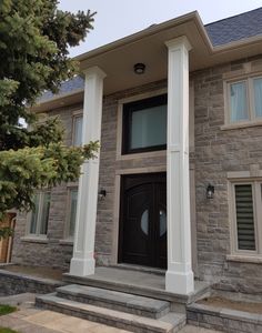 the front entrance to a house with two large pillars on each side and a black door