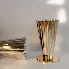 a gold vase sitting on top of a white table next to a silver plate and another metal object