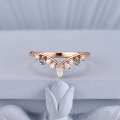 a rose gold ring with green and white stones on the side, sitting on top of a