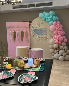 a table topped with plates covered in paper flowers and palm leaf decorations next to balloons