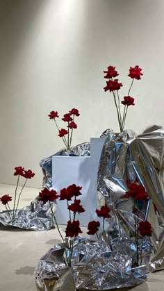 some red flowers are sitting in tinfoil on the floor and one is wrapped in silver foil