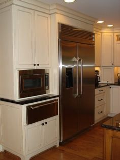 a kitchen with white cabinets and stainless steel appliances in the center, along with hardwood floors