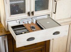 an open drawer in the middle of a kitchen counter with electronics plugged into it