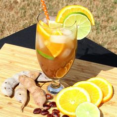 a glass filled with liquid sitting on top of a wooden table next to sliced lemons