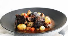 a black plate topped with meat and potatoes on top of a white cloth next to a knife