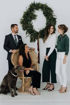 three people and a dog are standing in front of a christmas wreath with a wreath on the wall behind them