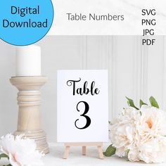 a table number sign sitting on top of a wooden easel next to white flowers