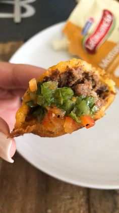 a person holding up a piece of food on a white plate next to some chips