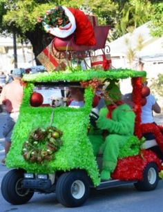 a car decorated with green grass and santa clause riding down the street in a parade