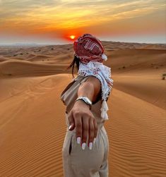 a woman standing in the desert with her hand out to the sun setting behind her