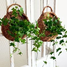 two wicker baskets with green leaves hanging from the side of a white door,