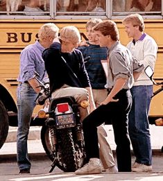 several people standing around a parked motorcycle in front of a school bus