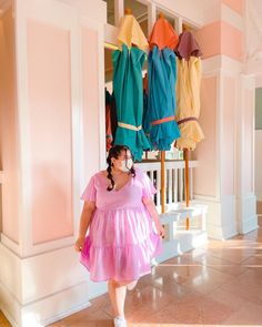 a woman in a pink dress standing next to a rack with umbrellas hanging from it