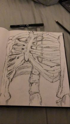 an open book with a drawing of a skeleton on it and a pen next to it