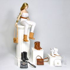 a doll sitting on top of a white pedestal next to shoes and handbages