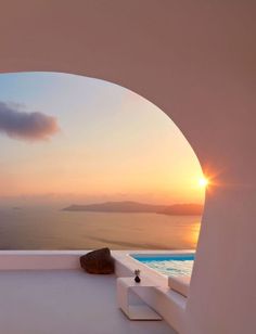 the sun is setting over an ocean view from a house with white walls and windows