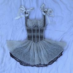 a crocheted dress is laying on a white sheet with ribbon around the waist