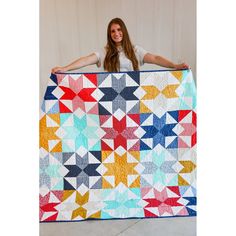 a woman holding up a colorful quilt with stars on it