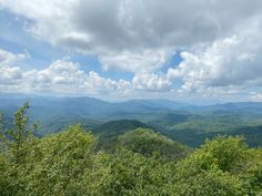 the mountains are covered in clouds and green foliage on a sunny day with blue skies