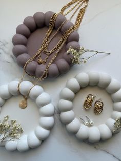 three necklaces and two rings on a marble counter top with gold chains around them