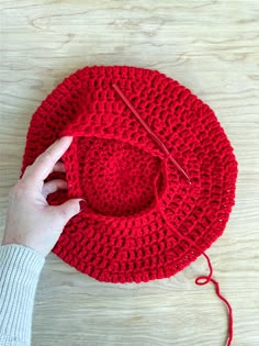 a person is knitting a red hat on a table with yarn and scissors next to it