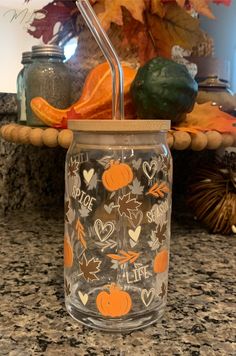 a glass cup with a straw in it sitting on a counter next to some pumpkins